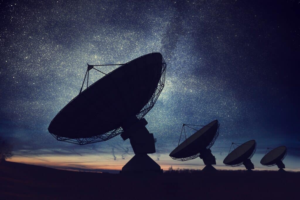 Stock image showing silhouettes of satellite dishes or radio antennas against night sky.