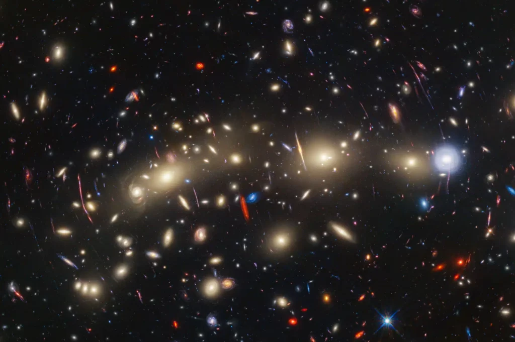 This panchromatic view of galaxy cluster MACS0416 was created by combining infrared observations from NASA’s James Webb Space Telescope with visible-light data from NASA’s Hubble Space Telescope.