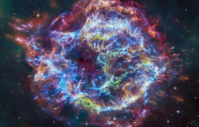 This image of Cassiopeia A resembles a disk of electric light with red clouds, glowing white streaks, red and orange flames, and an area near the center of the remnant resembling a somewhat circular region of green lightning.