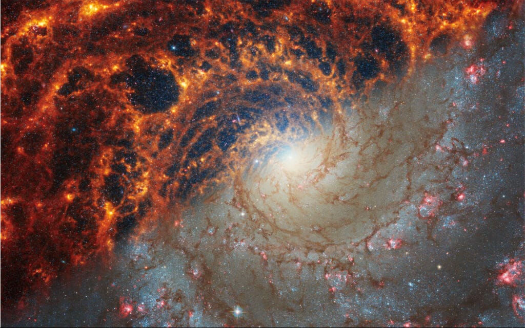 Face-on spiral galaxy, NGC 628, is split diagonally in this image: The James Webb Space Telescope’s observations appear at top left, and the Hubble Space Telescope’s on bottom right