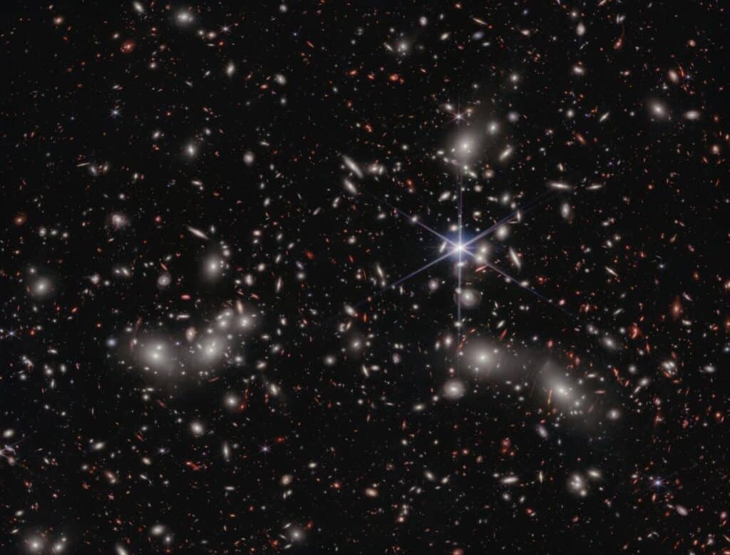 A crowded galaxy field on a black background, with one large star dominating the image just right of center